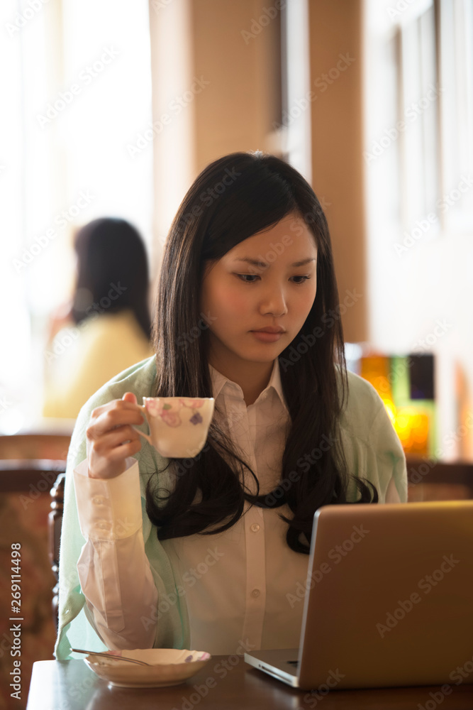 ティーカップを持ちパソコンの画面を見る女性 ティーカップを持ちパソコンの画面を見る女性