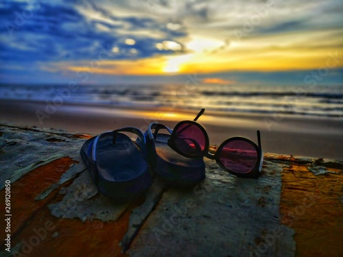 Beautiful sunset view with flip-flop and sunglasses on beach background.