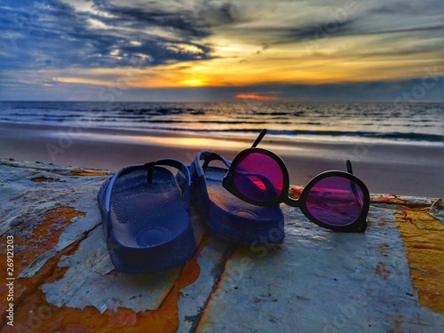 A beautiful nature photography of sunset view with flip-flop and sunglasses on beach background.