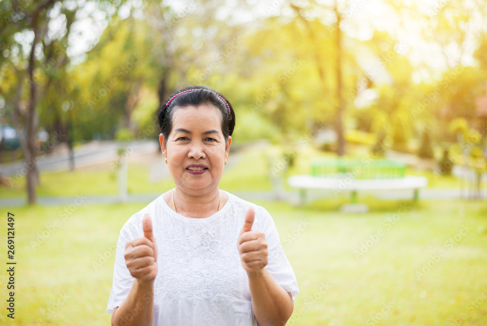 Portrait of a elderly asian woman standing and showing thumb up at park in the morning,Happy and smiling,Freedom time Portrait of a elderly asian woman standing and showing thumb up at park in the morning,Happy and smiling,Freedom time