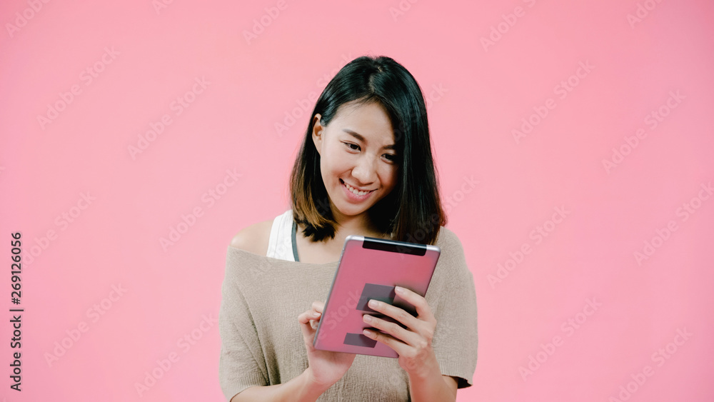 Young Asian woman using tablet checking social media feeling happy smiling in casual clothing over pink background studio shot. Happy smiling adorable glad woman rejoices success. Young Asian woman using tablet checking social media feeling happy smiling in casual clothing over pink background studio shot. Happy smiling adorable glad woman rejoices success.