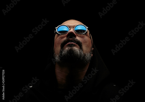 Bald man with a gray beard in sunglasses on a dark background. The concept of hope.