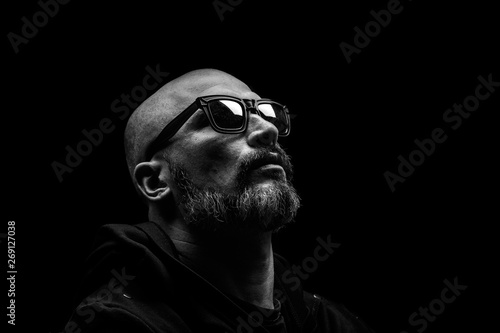Bald man with grey beard in sunglass on dark background