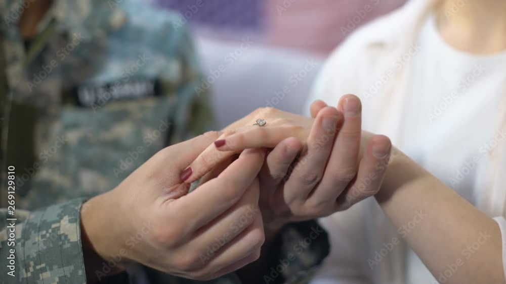 Male soldier putting engagement ring on girlfriends finger, happy marriage Male soldier putting engagement ring on girlfriends finger, happy marriage