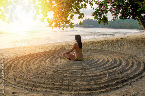 the girl sits back on the sandy beach in the center of an impromptu circle and meditates