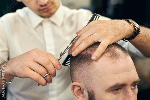 Cropped of man professional hairdresser barber making short haircut for his client in modern barbershop. Concept of traditional haircutting with scissors. Creating men's hairstyles.