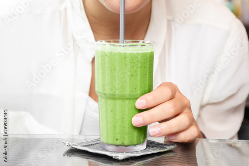 Matcha green tea smoothie cold dessert shake drink woman drinking with straw at cafe table.