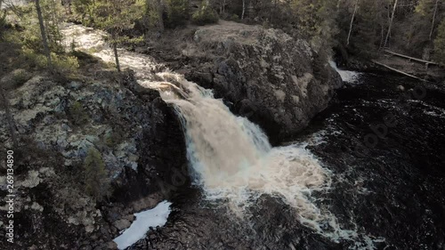 Aerial, descending, drone shot, tilting towards the Komulankongas waterfall, in middle of pine and spruce forest, on a sunny spring day, in Hyyrynsalmi, Kainuu, Finland photo