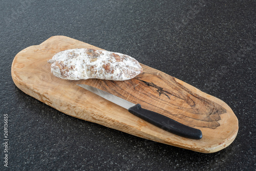 Dried sausage and a knife on wood on a black table close-up view