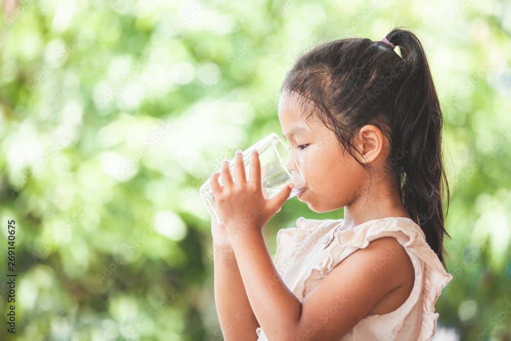 Cute asian child girl drinking fresh water from glass on green nature background Cute asian child girl drinking fresh water from glass on green nature background
