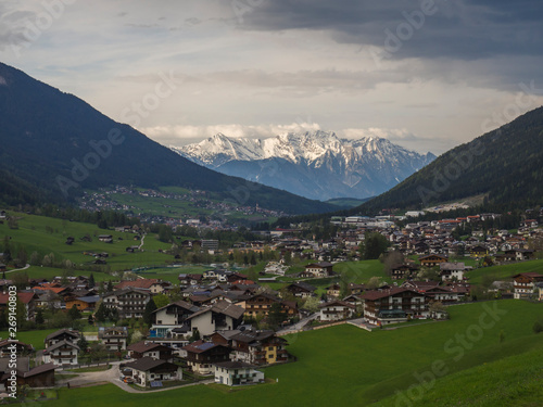 Spring mountain rural landscape. View over Stubaital Stubai Valley near Innsbruck  Austria with village Neder  green meadow  forest  snow covered alpen mountain peaks  evening dramatic clouds and