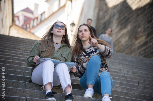 Two young women sitting on stairs holding a map and looking straight