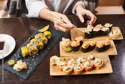 Four course lunch on special offer in luxury oriental restaurant. Elegant girl wrapped in blanket tasty delicious sushi set with seafood. Woman in white blouse eating Japanese dish using food sticks.