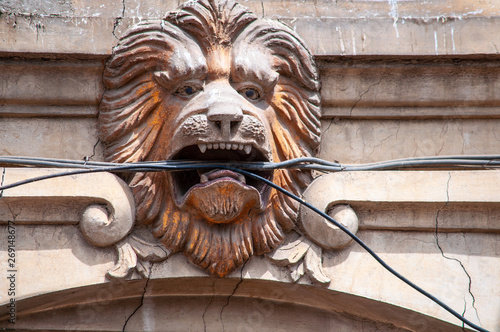 The lion head on the front of the building holding electric cable in open mouth photo