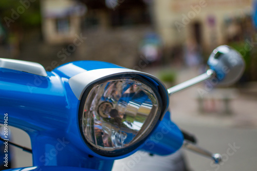 Close up of the headlight of a blue classic scooter (vespa) with defocused background
