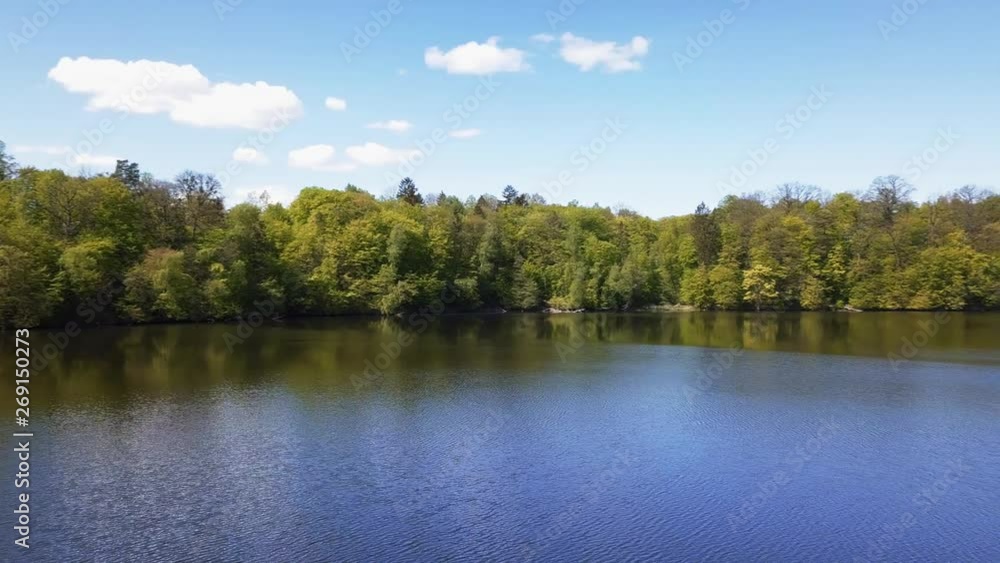 Aerial. Small lake surrounded by green trees. Shot from a low flying drone. Pan shot. Spring 2019. Aerial. Small lake surrounded by green trees. Shot from a low flying drone. Pan shot. Spring 2019.