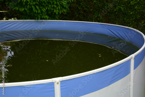 messy lost place blue-white pool background, unkempt frame swimming pool with green colored water due to algae and dirt