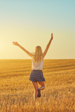 Cute young woman jumping in a wheat field.