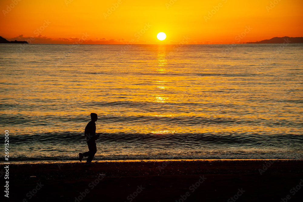 夕日に輝く海の砂浜を走る人