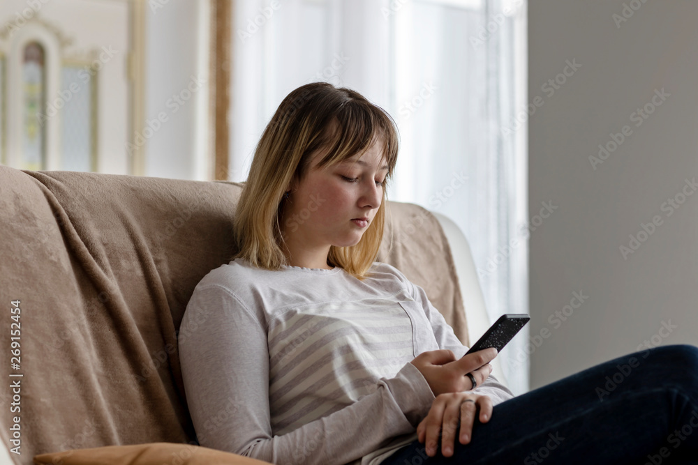 Girl teenager sitting on the couch in the room, looking into the phone and listening to music on headphones. Girl teenager sitting on the couch in the room, looking into the phone and listening to music on headphones.