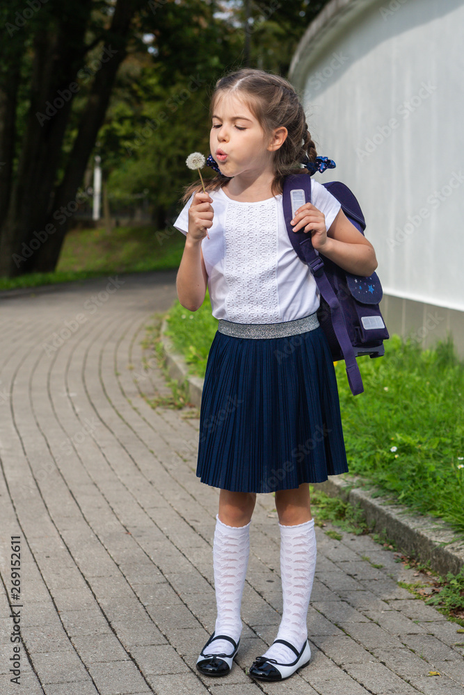 beautiful schoolgirl blowing on a dandelion in the park