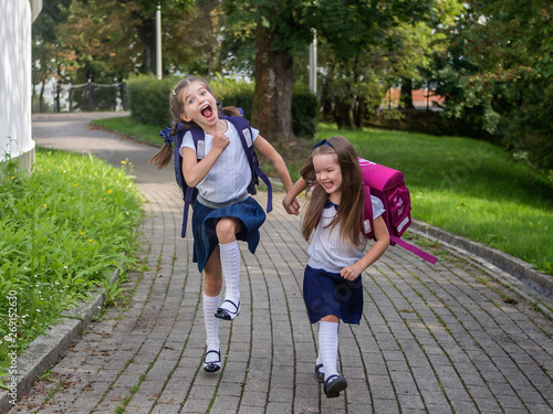 two happy schoolgirls hold hands and run to school, September 1 and back to school concept, school break, school holidays