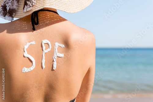 Young girl has spf word on her back made of sun cream at the beach. Sun protection factor concept photo