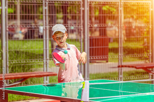 Cute little boy playing table tennis in park – outdoor activity in sport ground with smiling kid having fun learning and practicing ping pong hitting the ball – healthy activity for child