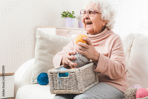 Smiling eldery woman with white basket holding colorful laces balls photo