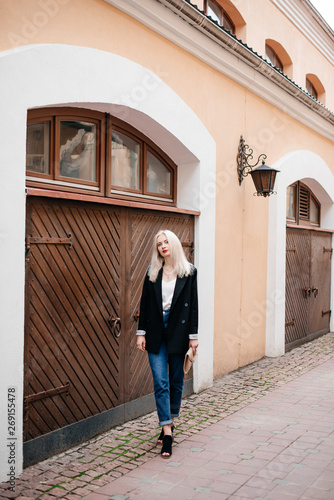 Outdoor portrait of beautiful young woman with blonde hair. Stylish girl in a black jacket and blue jeans posing on the street. Fashion model