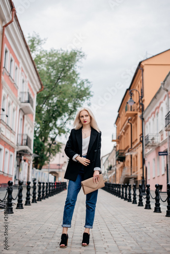 Outdoor portrait of beautiful young woman with blonde hair. Stylish girl in a black jacket and blue jeans posing on the street. Fashion model