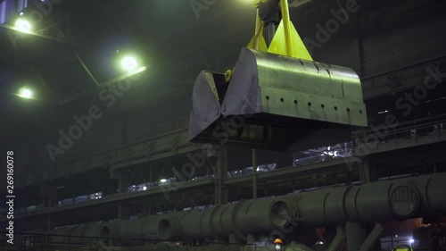 In a dark factory floor a large yellow open two-leaf grab is advanced
