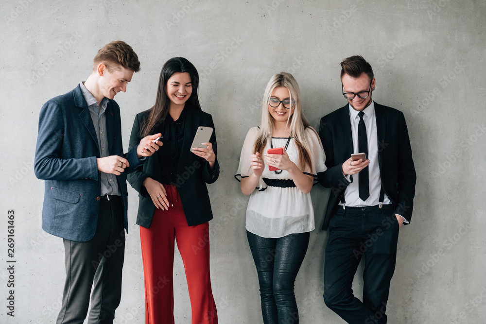 Social media addiction. Modern lifestyle. Young colleagues leaning on wall, using smartphones and internet to share fun content. Social media addiction. Modern lifestyle. Young colleagues leaning on wall, using smartphones and internet to share fun content.
