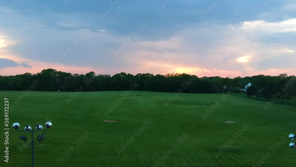 drone shot of a driving range during a colorful sunset. As the camera gets higher, more of the sky and surrounding neighborhood can be seen. drone shot of a driving range during a colorful sunset. As the camera gets higher, more of the sky and surrounding neighborhood can be seen.