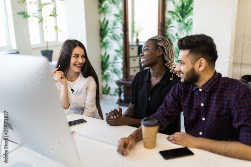 International confident team leader mentor use computer sitting together with diverse female colleagues at desk helping explaining to new employees corporate program giving instructions