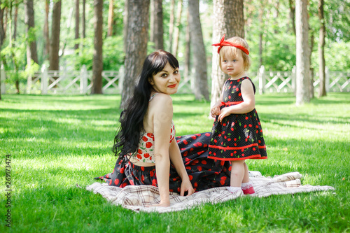 Happy mother and daughter in same dresses play in summer park under the trees shade of a beautiful green grass. Childhood. Concept of a happy family. Universal Children's Day