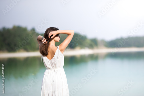 Young very beautiful girl with long hair in a white dress by the lake. The girl is enjoying the rest.