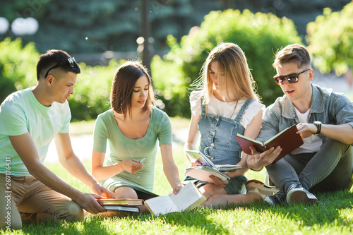 Group of students learning a lesson outdoors. Students reading text books or tutorial. Youth studying in the park.