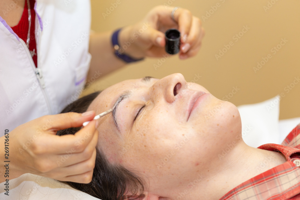 Beautician paint the eyebrows of a young woman