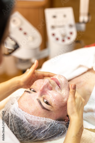Beautician make a facial treatment in the spa center. Young woman with facial cosmetic treatment