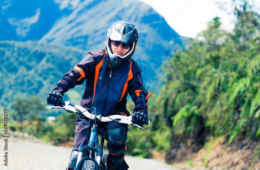 Naklejka premium Girl in special suit and equipment riding a bike on the background of mountains