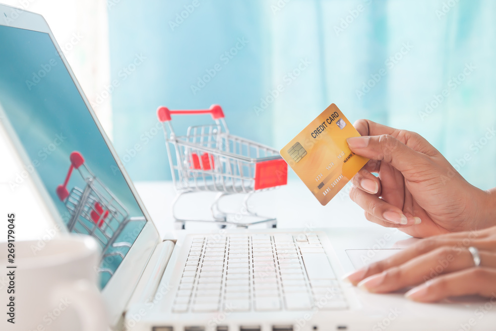Hands holding credit card and using laptop computer with shopping cart background. Online shopping, E-payment or internet banking