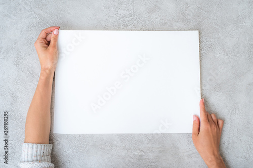 Girl's hands horizontally holding a big white sheet of paper