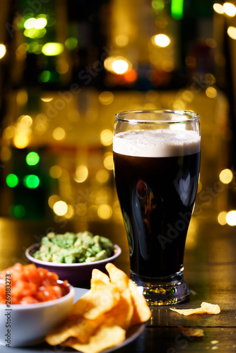 Glass of stout with nachos, tomato salsa and guacamole. Bar bottles in bokeh, high resolution photo