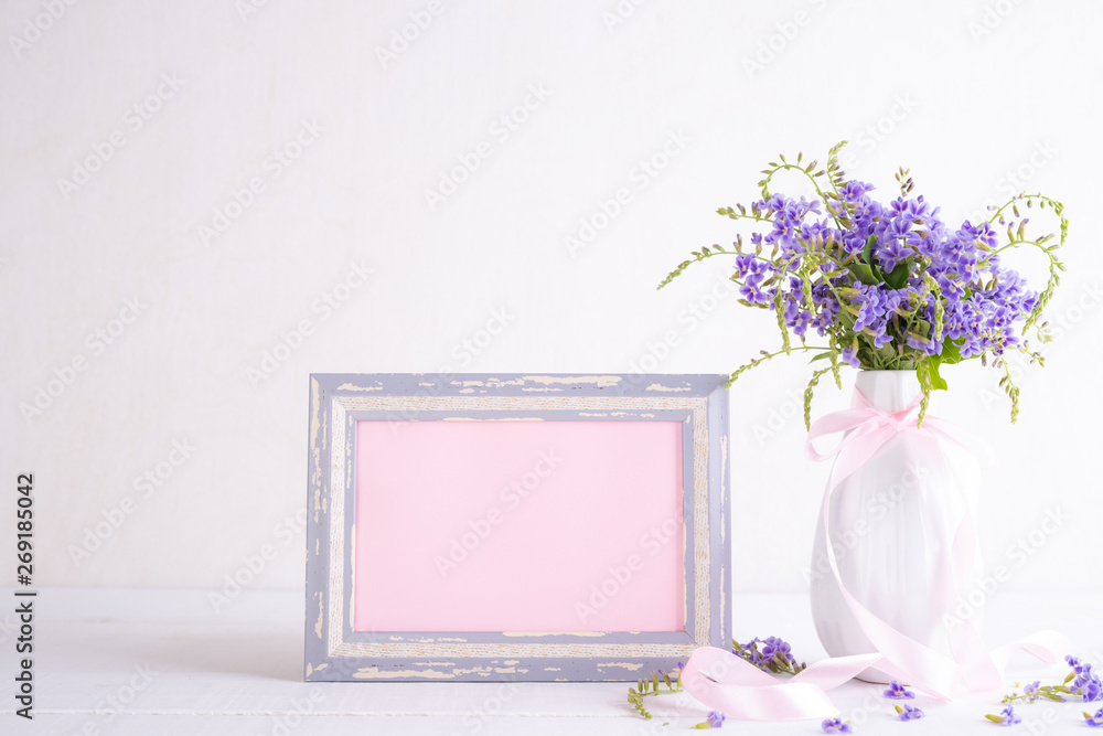 White picture frame with lovely purple flower in vase on white wooden table. White picture frame with lovely purple flower in vase on white wooden table.