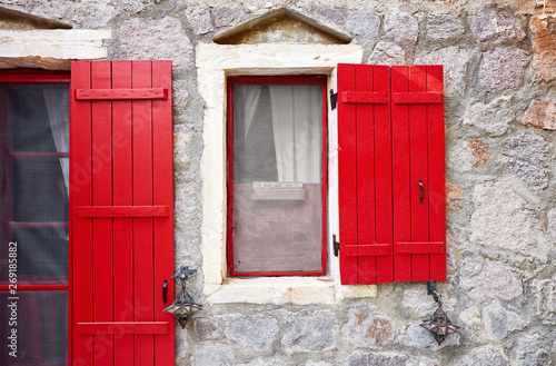 Red wooden shutters and the window of a stone house