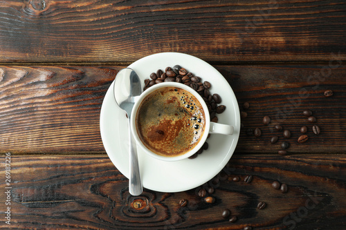 Cup of coffee with spoon and coffee beans on wooden background, space for text and top view
