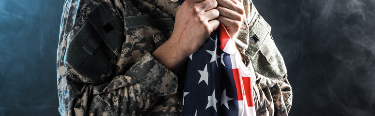 Panoramic shot of soldier holding American flag on black with smoke