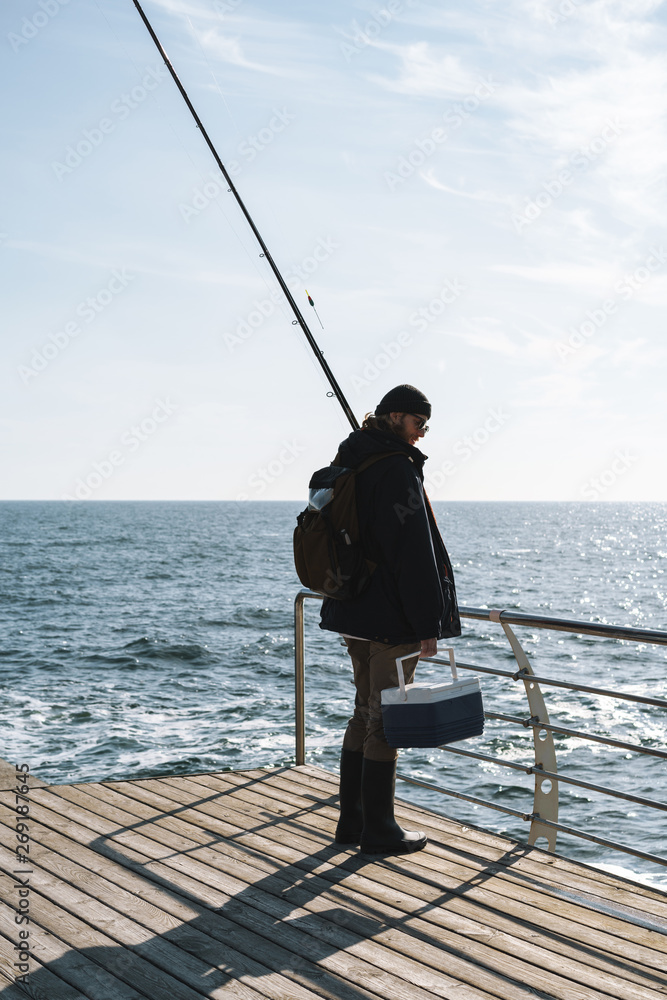 Silhouette of man fisherman wearing coat, holding rod