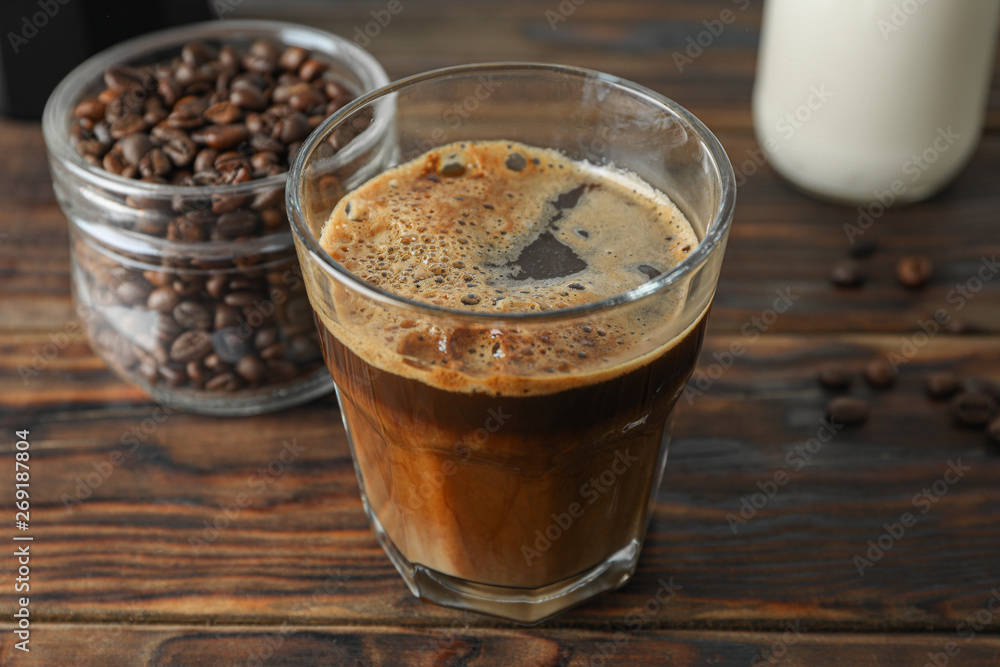 Glass of fresh coffee and coffee beans on wooden table, space for text Glass of fresh coffee and coffee beans on wooden table, space for text